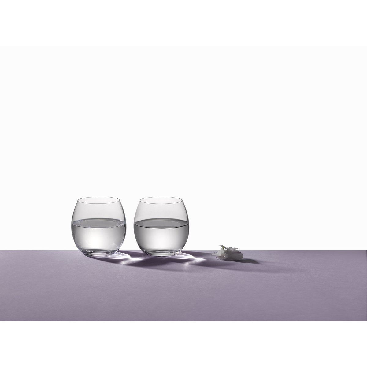 Two clear glasses filled with water on a light purple surface.