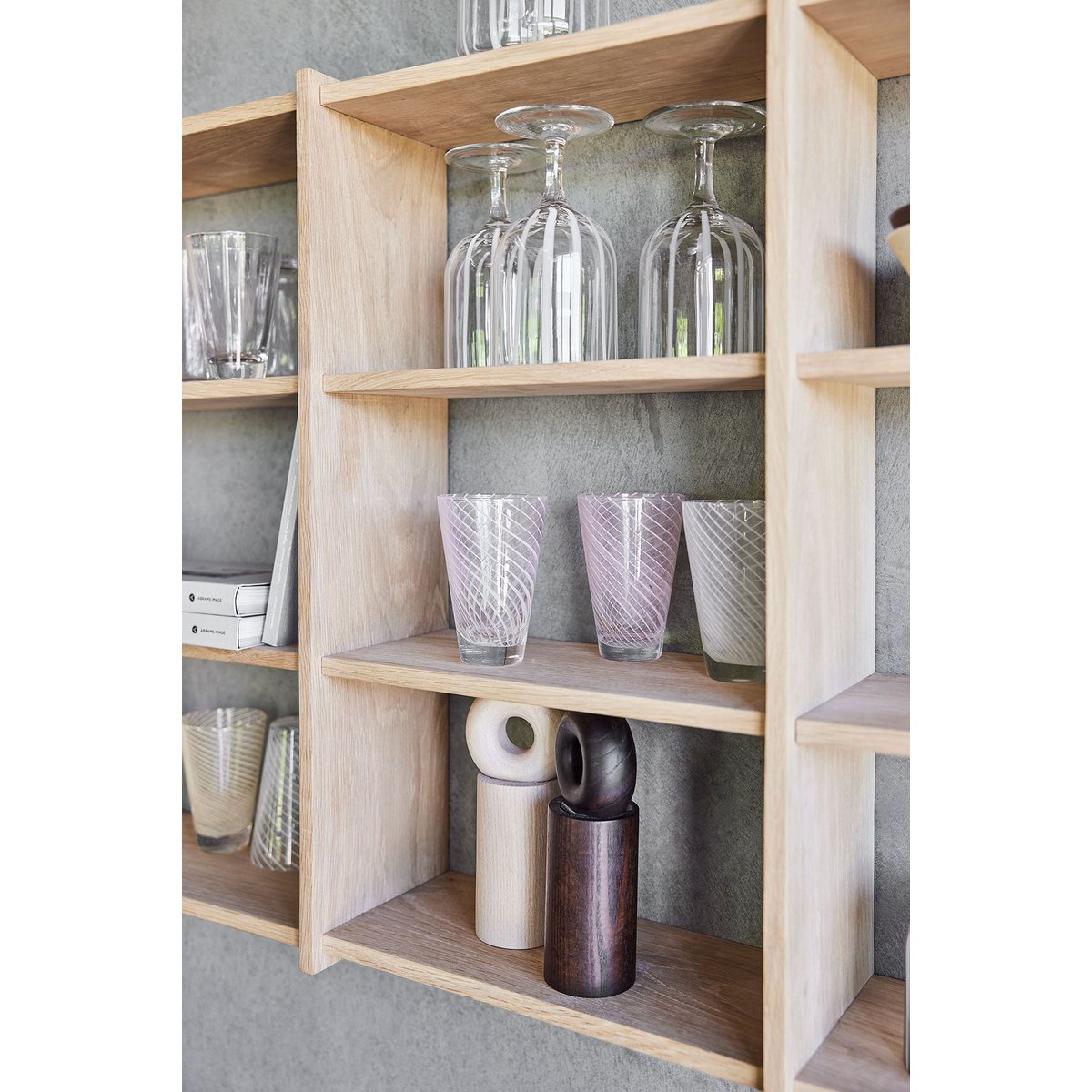 Wooden shelf with glassware and decorative items against a gray wall.