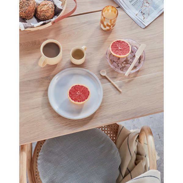 Table setting with grapefruit halves, coffee cups, and a basket of bread on a wooden table.