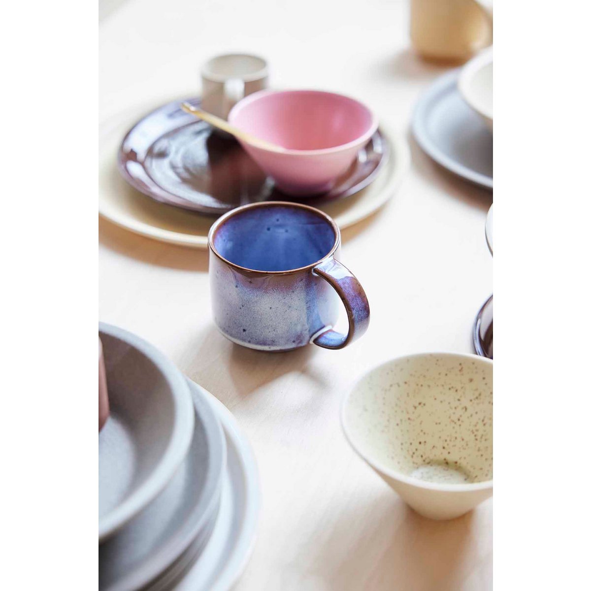 Collection of ceramic mugs and bowls on a light wooden surface