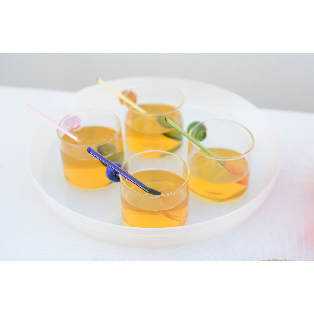 Four glasses of orange juice with straws on a white surface