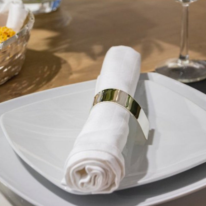 White napkin with a gold ring on a white plate on a wooden table.