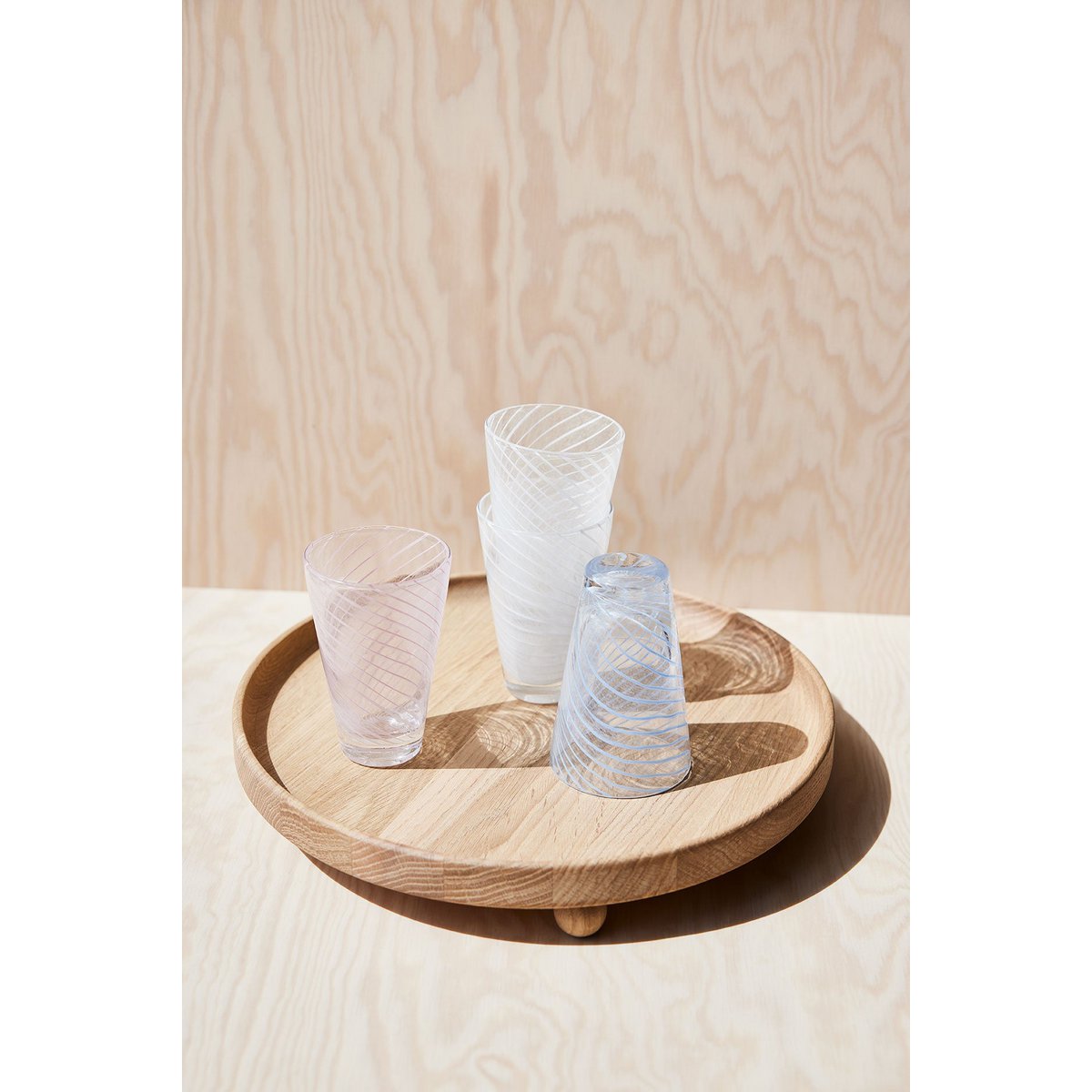 Three glass tumblers on a wooden tray against a light wood panel background