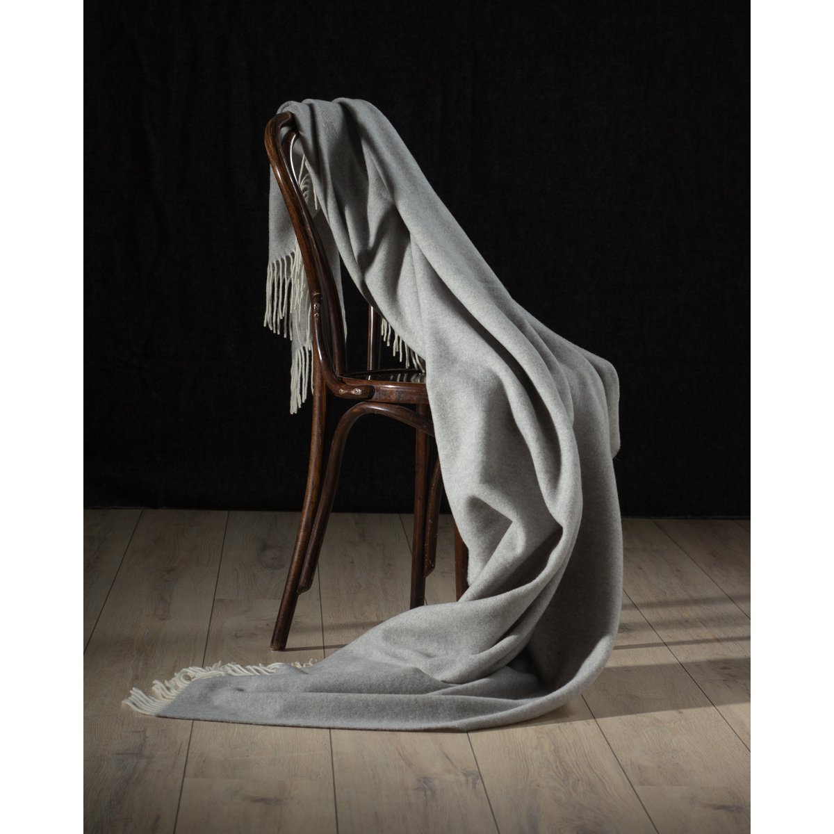 Gray throw blanket draped over a wooden chair against a dark background