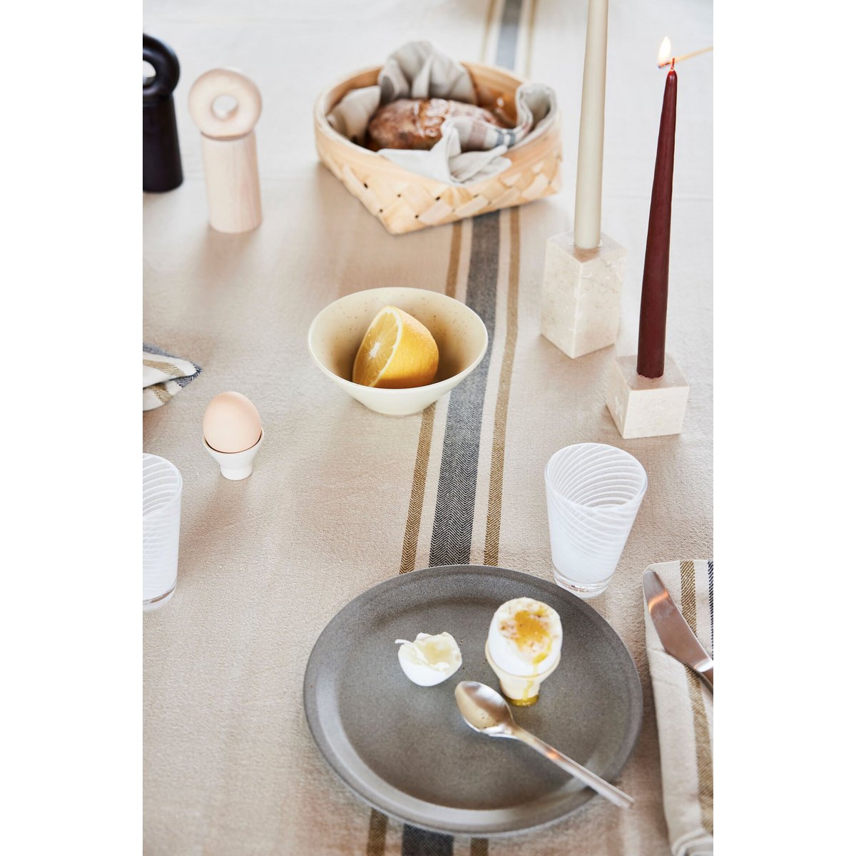 Table setting with a bowl of lemons, a plate with a soft-boiled egg, and a lit candle in a stone candleholder.