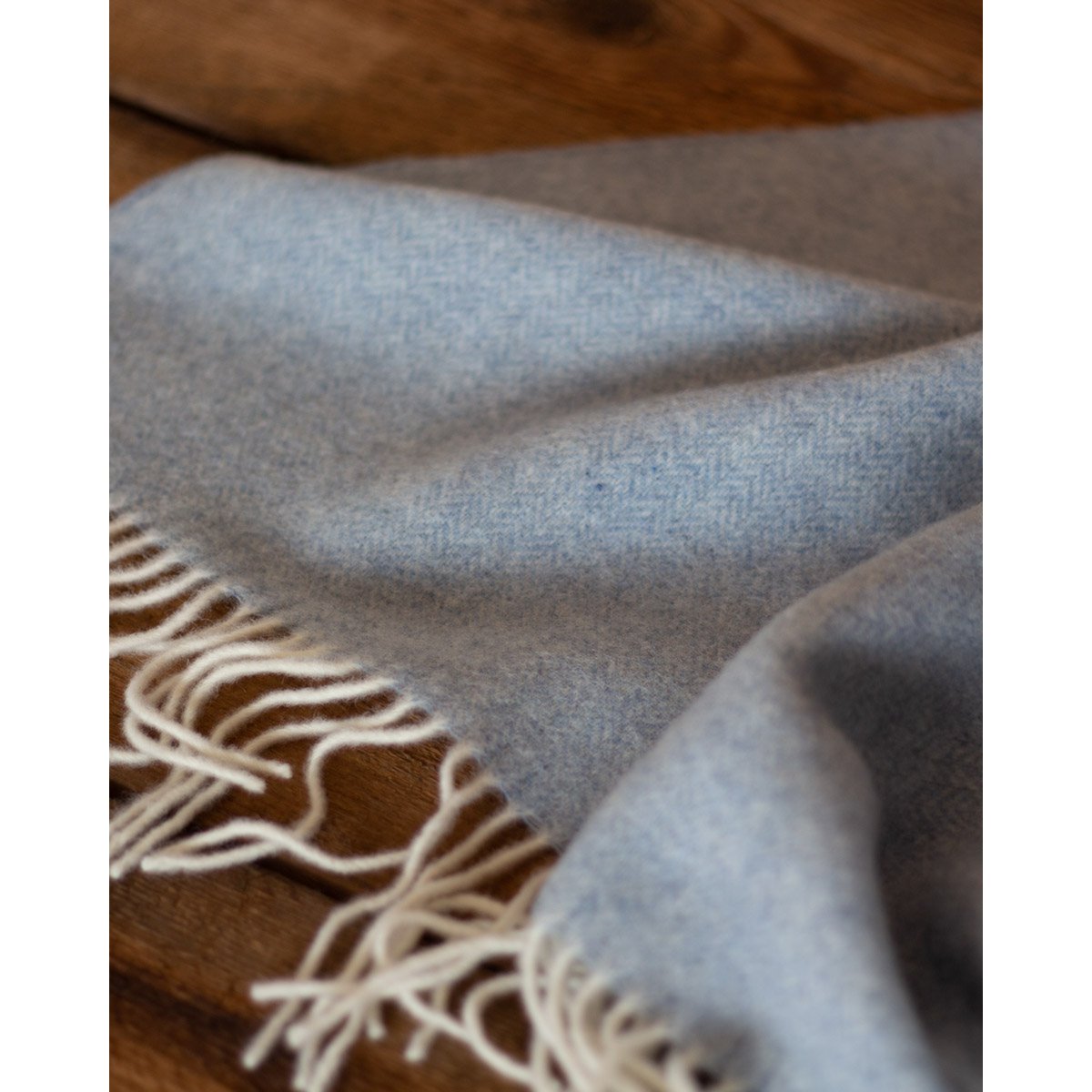 Gray blanket with white fringe on a wooden surface