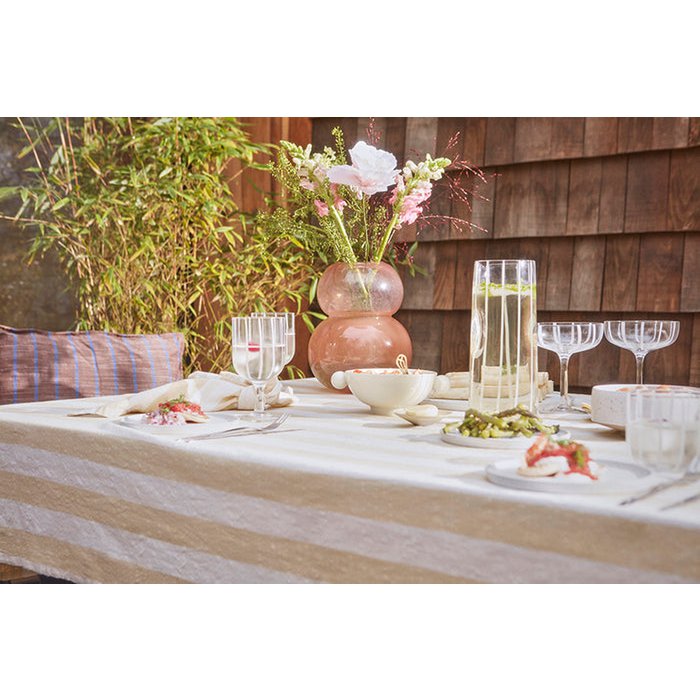 Dining table set with flowers, glasses, and plates outdoors.