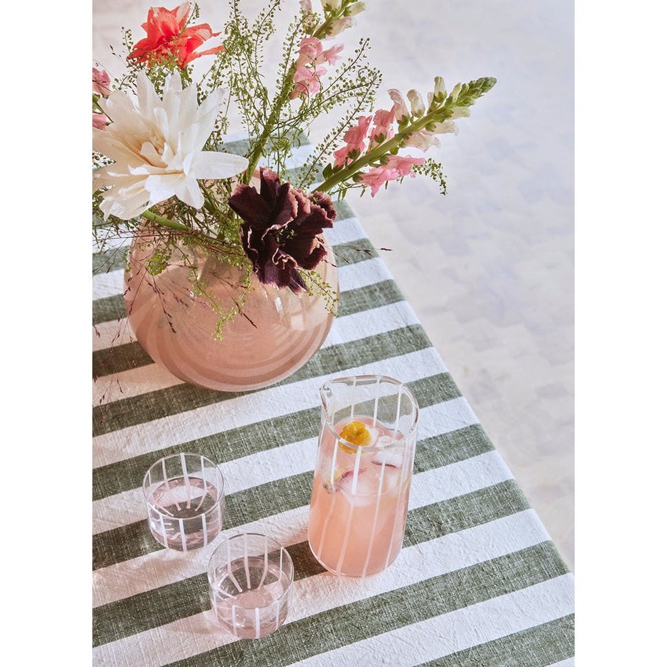 Vase with flowers on a striped tablecloth with glasses of pink drinks.
