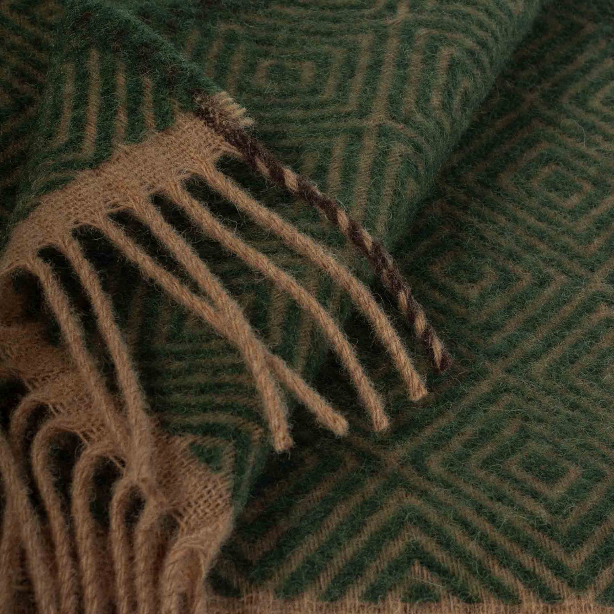 Close-up of a green and brown patterned fabric blanket with fringes