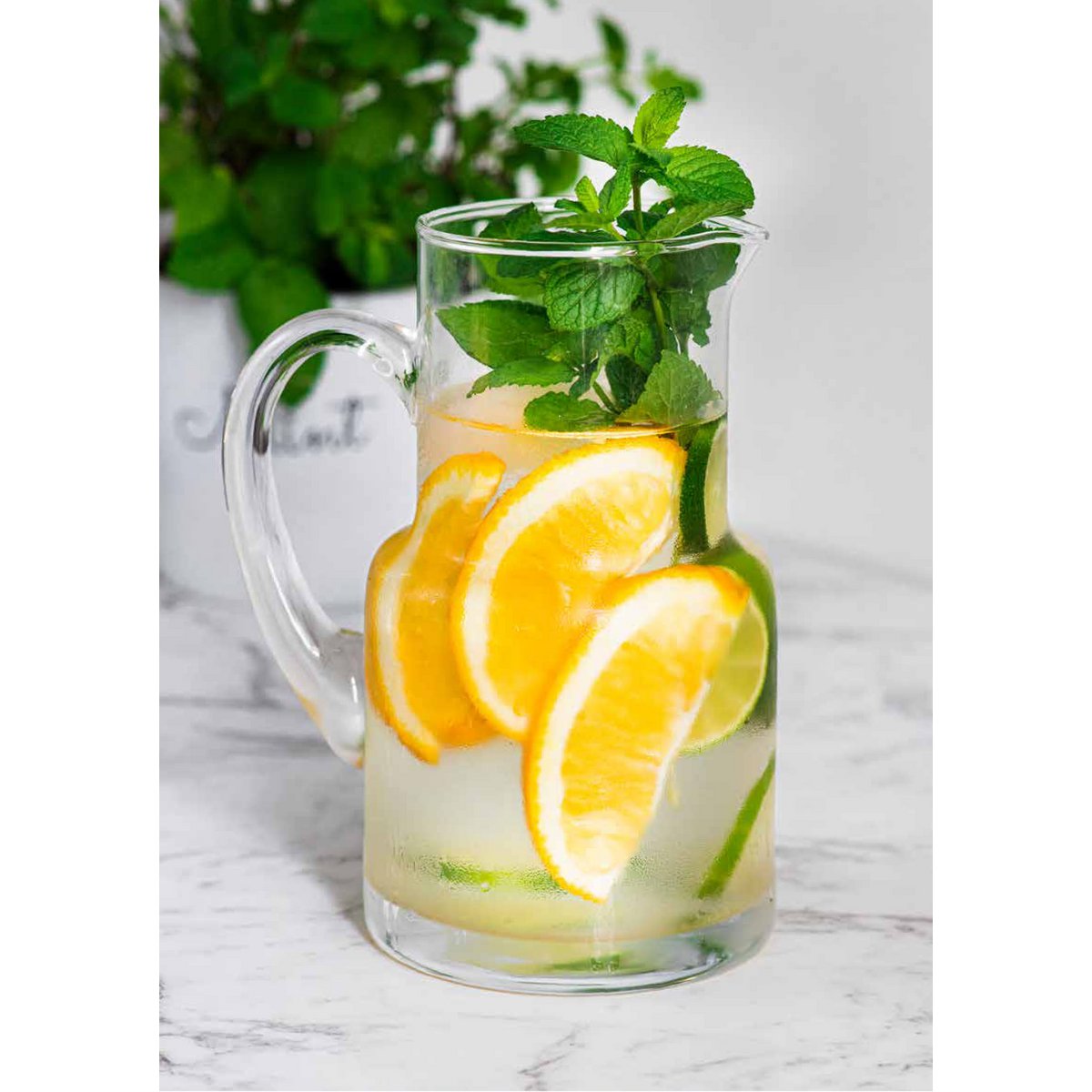 Glass pircher with lemon slices and mint leaves on a marble surface