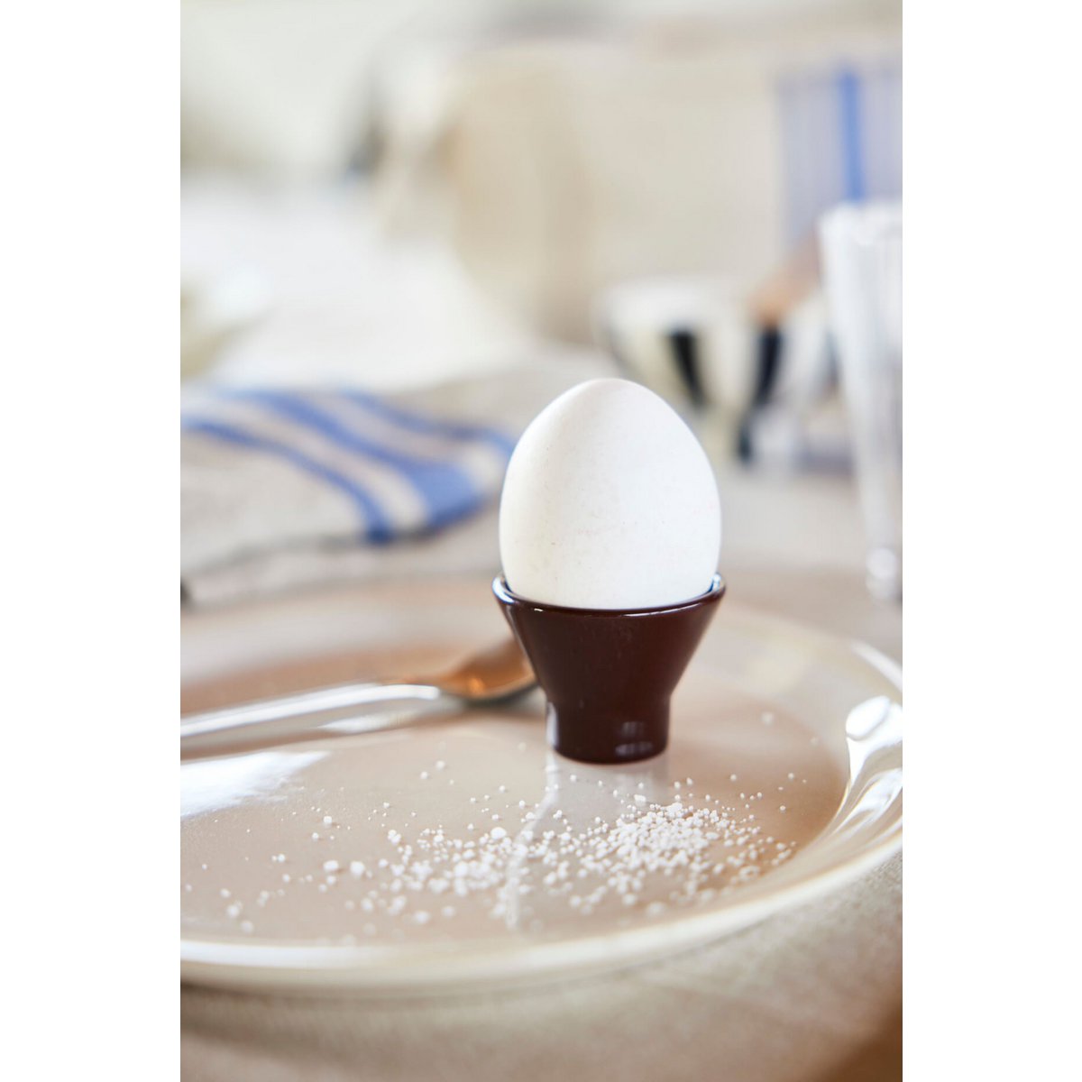 White egg in a brown holder on a white plate with a blurred background