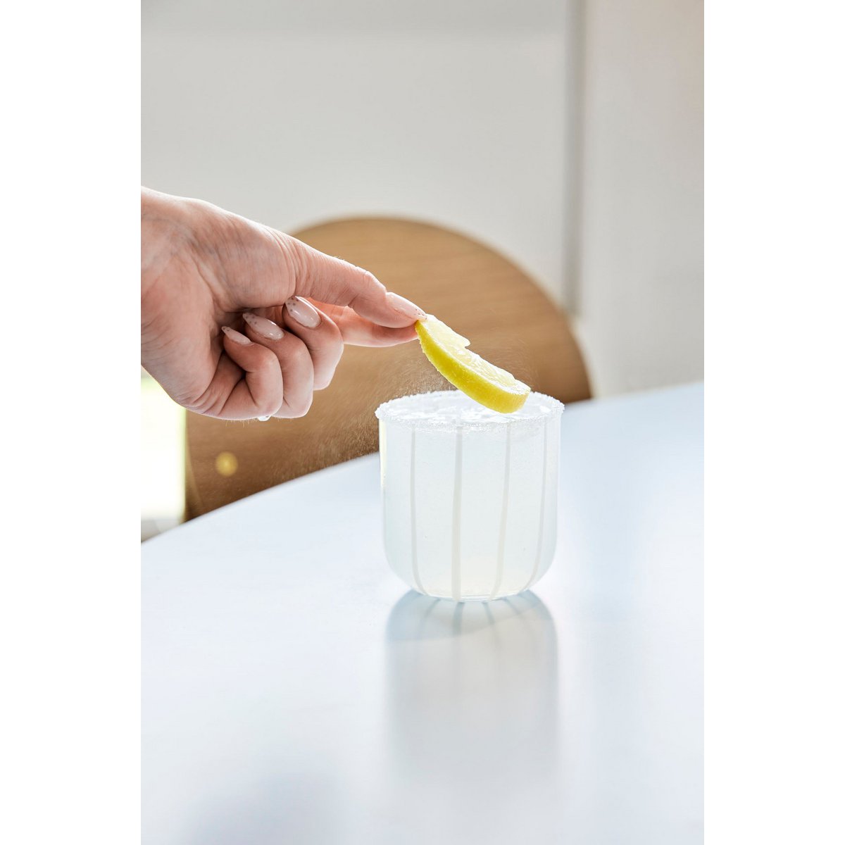 Person squeezing a lemon wedge into a clear glass on a white table.