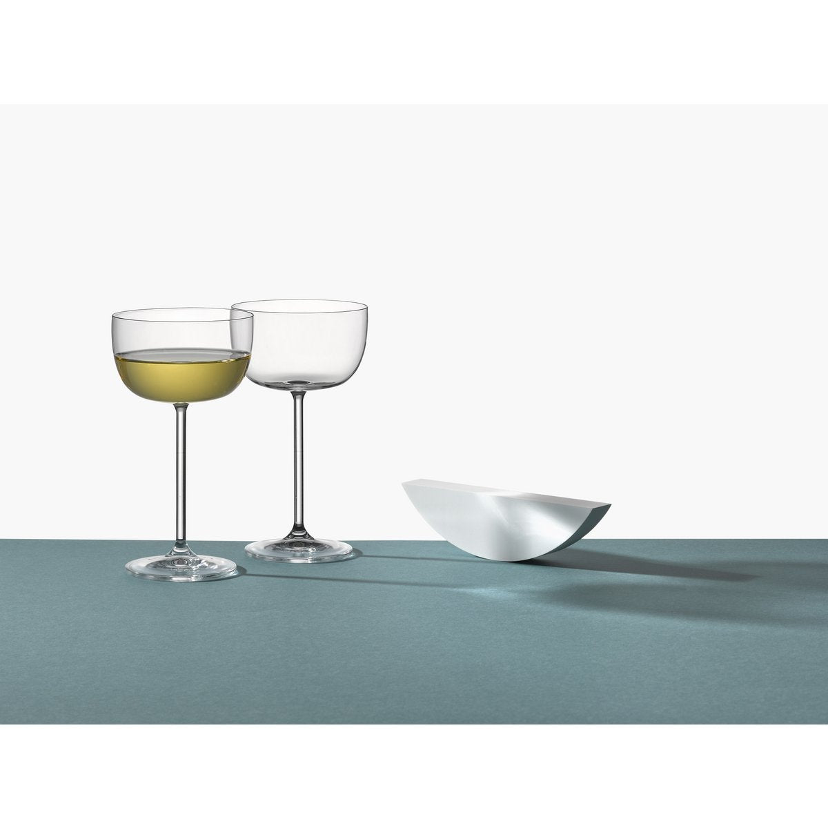 Two wine champagne glasses with a small bowl on a light grey surface