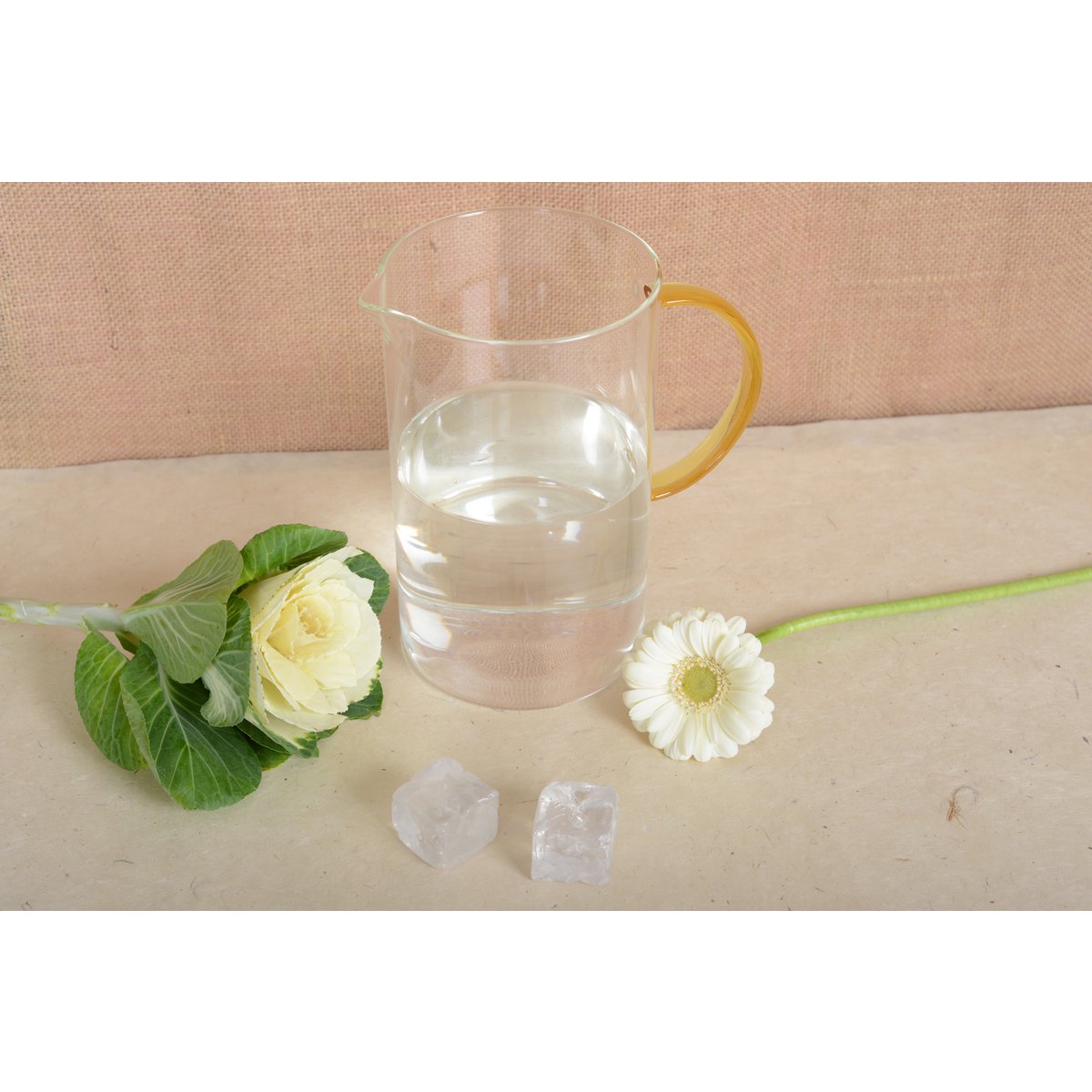 Clear glass pitcher with water, flowers, and crystals on a beige surface