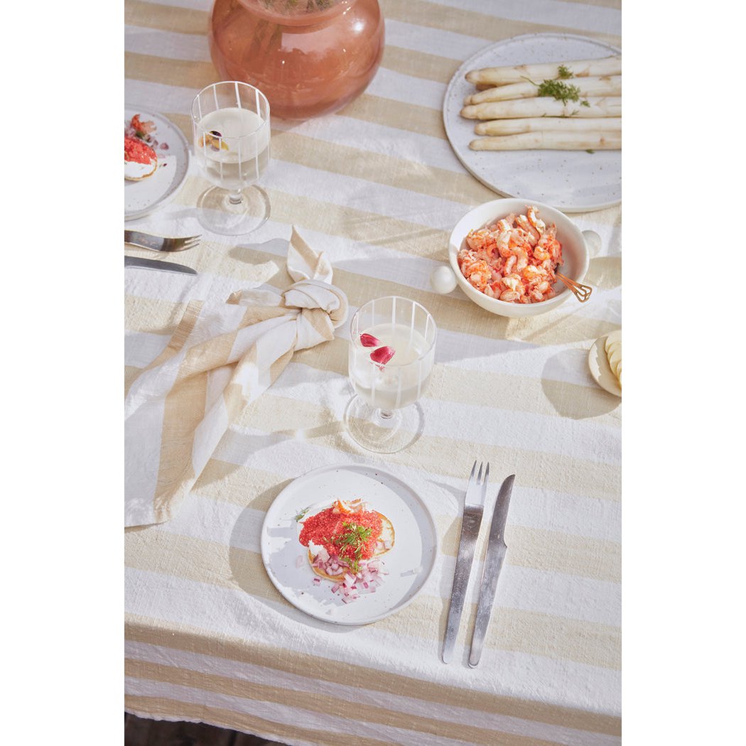 Dining table setting with plates of food and glasses on a striped tablecloth.