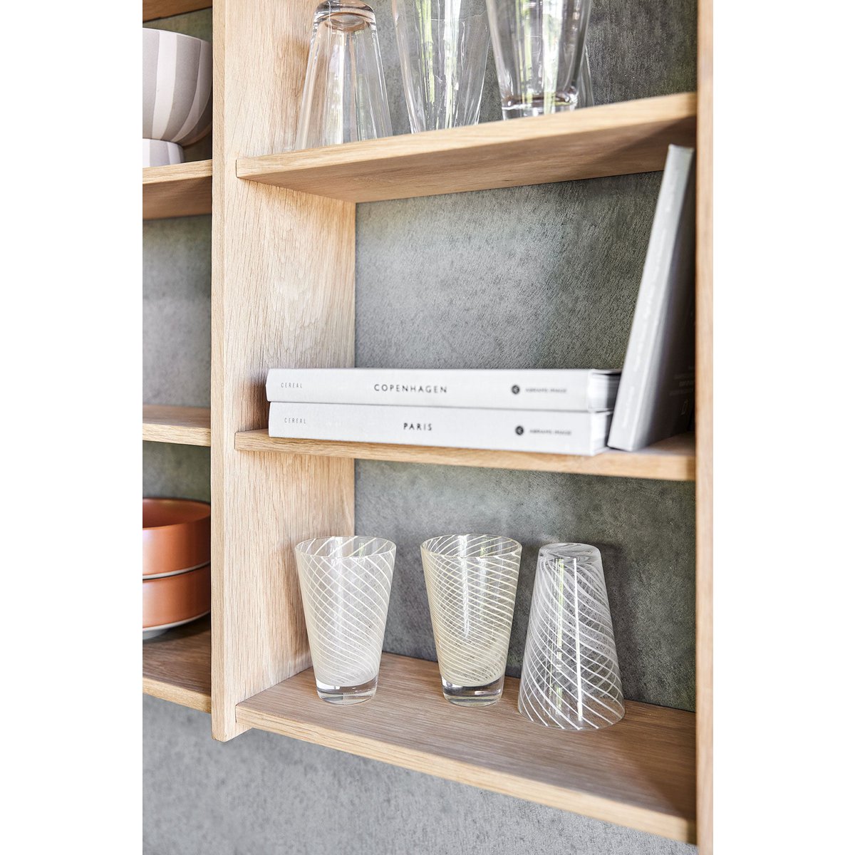 Wooden shelf with books and glass items against a grey wall.
