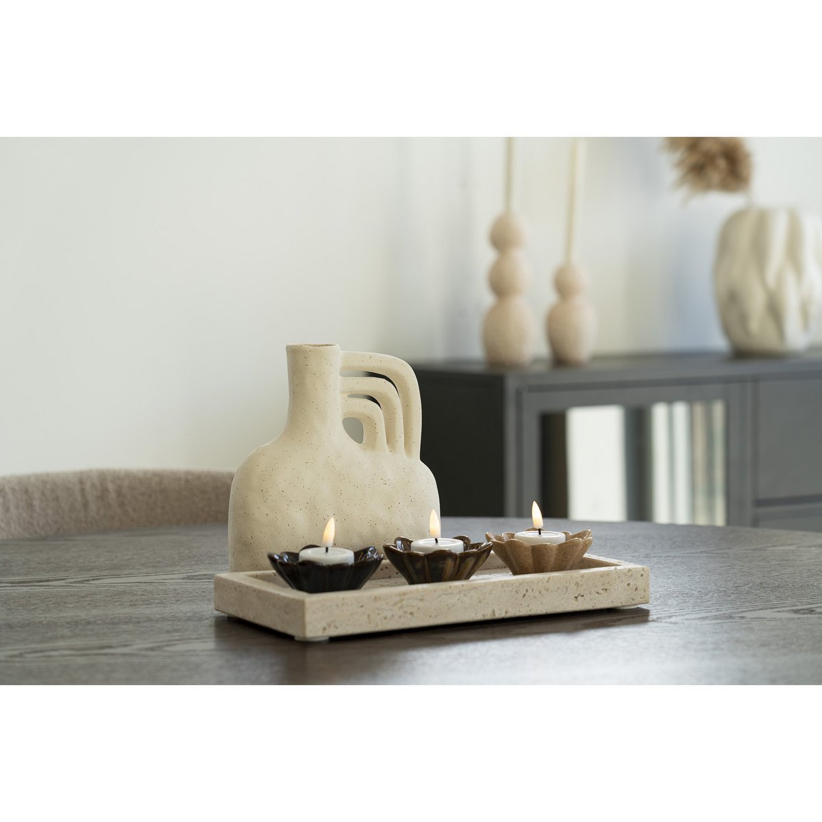 Decorative ceramic vase with lit candles and travertine stone tray on a wooden surface