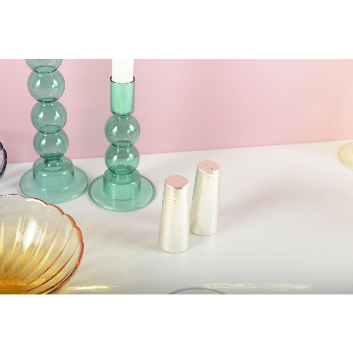 Green glass candle holders on a white surface with a pink background