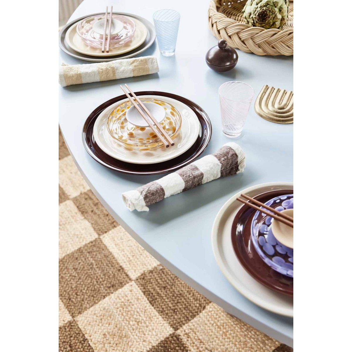 Dining table setting with plates, glasses, and napkins on a light blue surface.