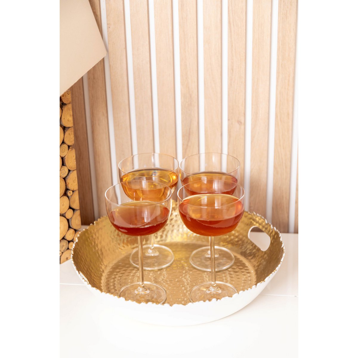 Four cocktail glasses with a golden rim on a decorative tray against a curtain background