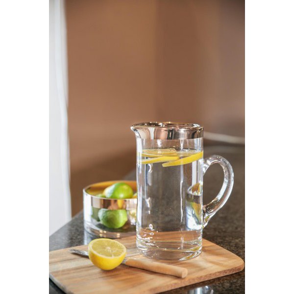 Clear glass pitcher with water and lemon slices on a wooden cutting board.