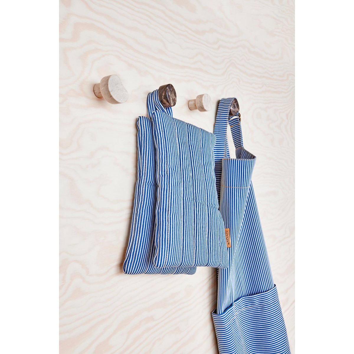 Blue striped aprons hanging on wooden hooks against a light wooden panel background