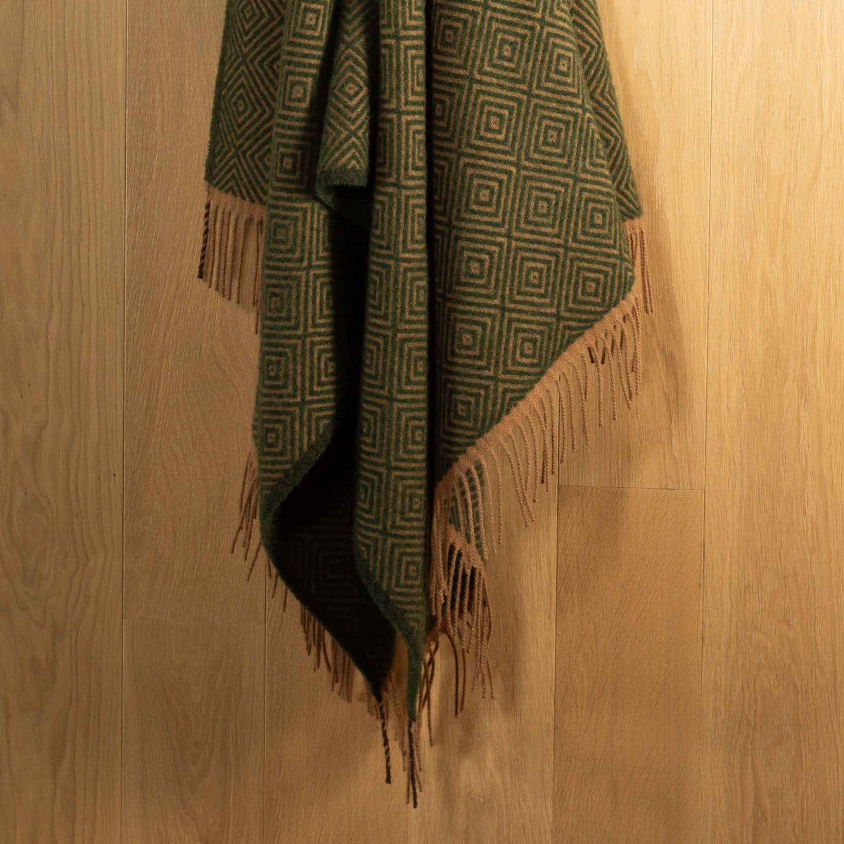 Green patterned blanket with fringes on a wooden surface