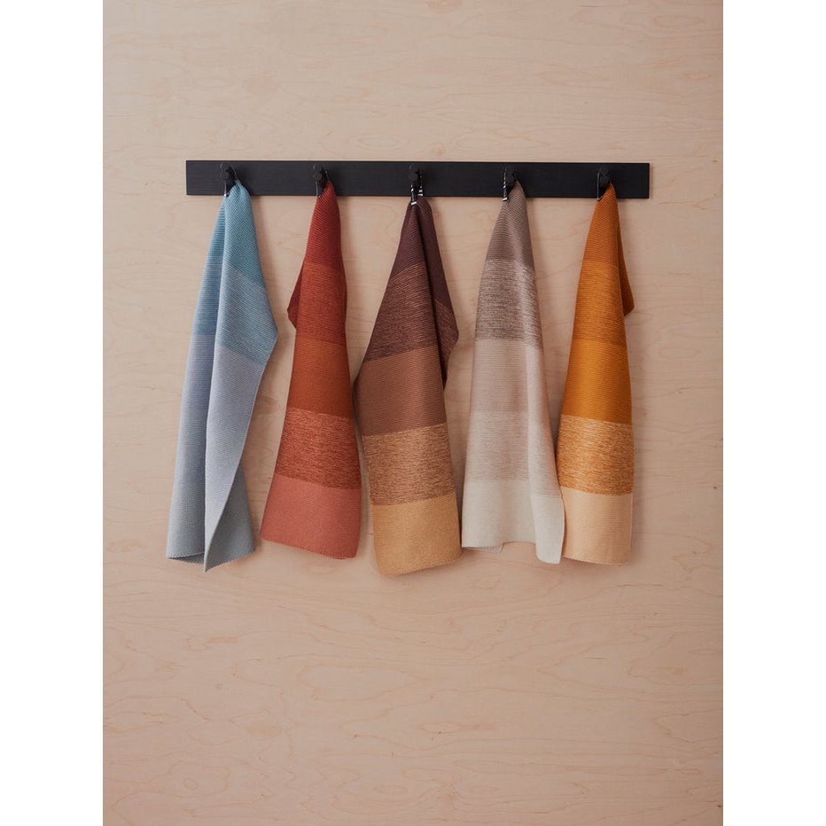 Set of five colorful towels hanging on a black rack against a beige wall.