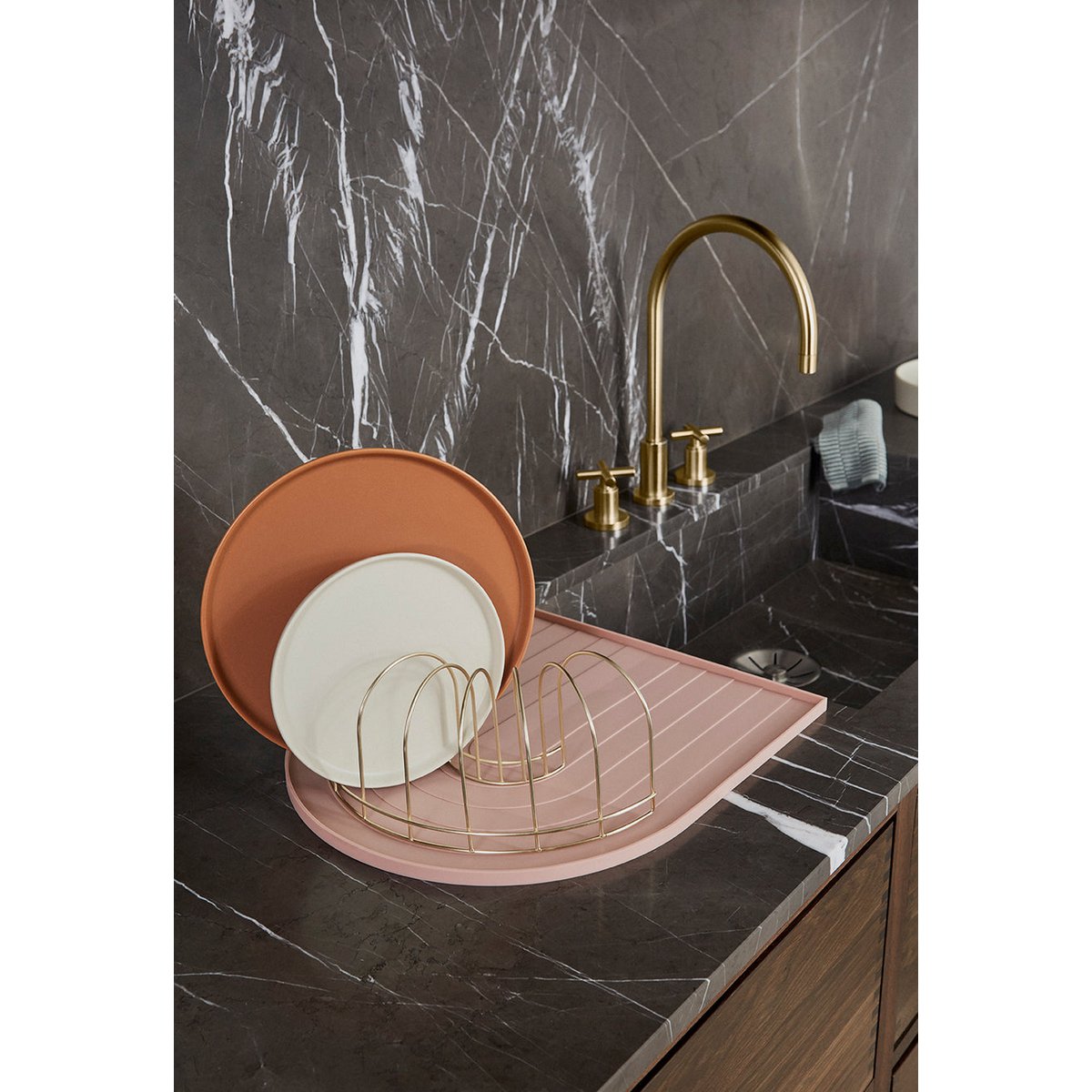 Kitchen sink area with marble backsplash, gold faucet, and pink dish rack.