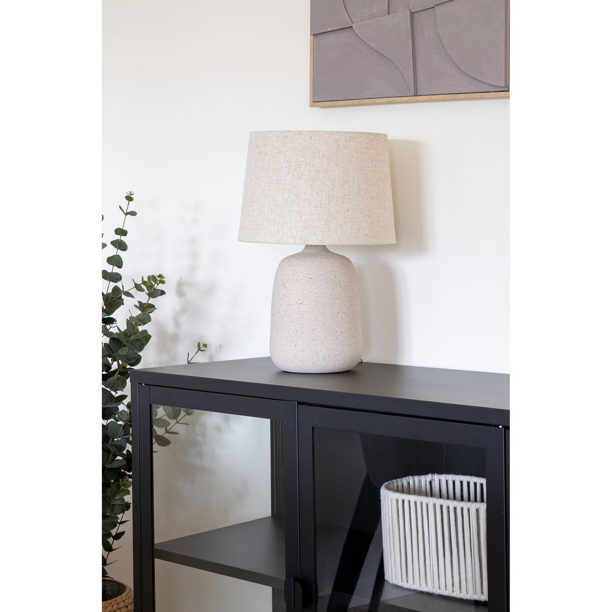 Table lamp with a textured base on a black cabinet against a white wall.