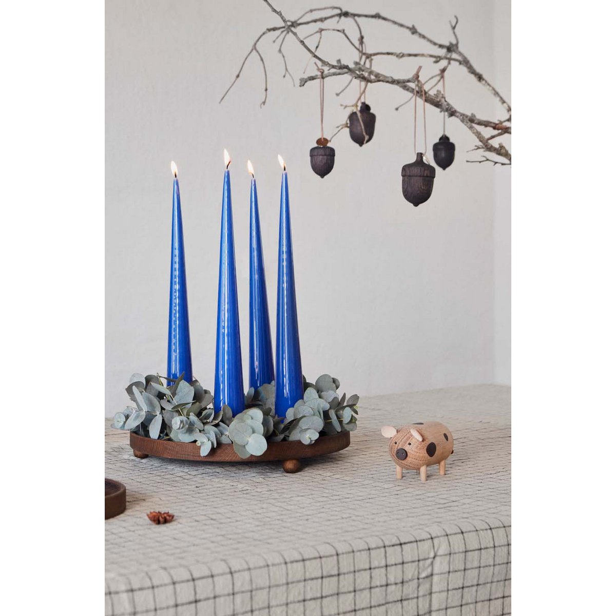 Decorative setup with blue candles in a holder, eucalyptus leaves, and a small pig figurine on a surface.