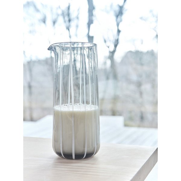 Clear glass pitcher with white liquid on a light surface, blurred outdoor background