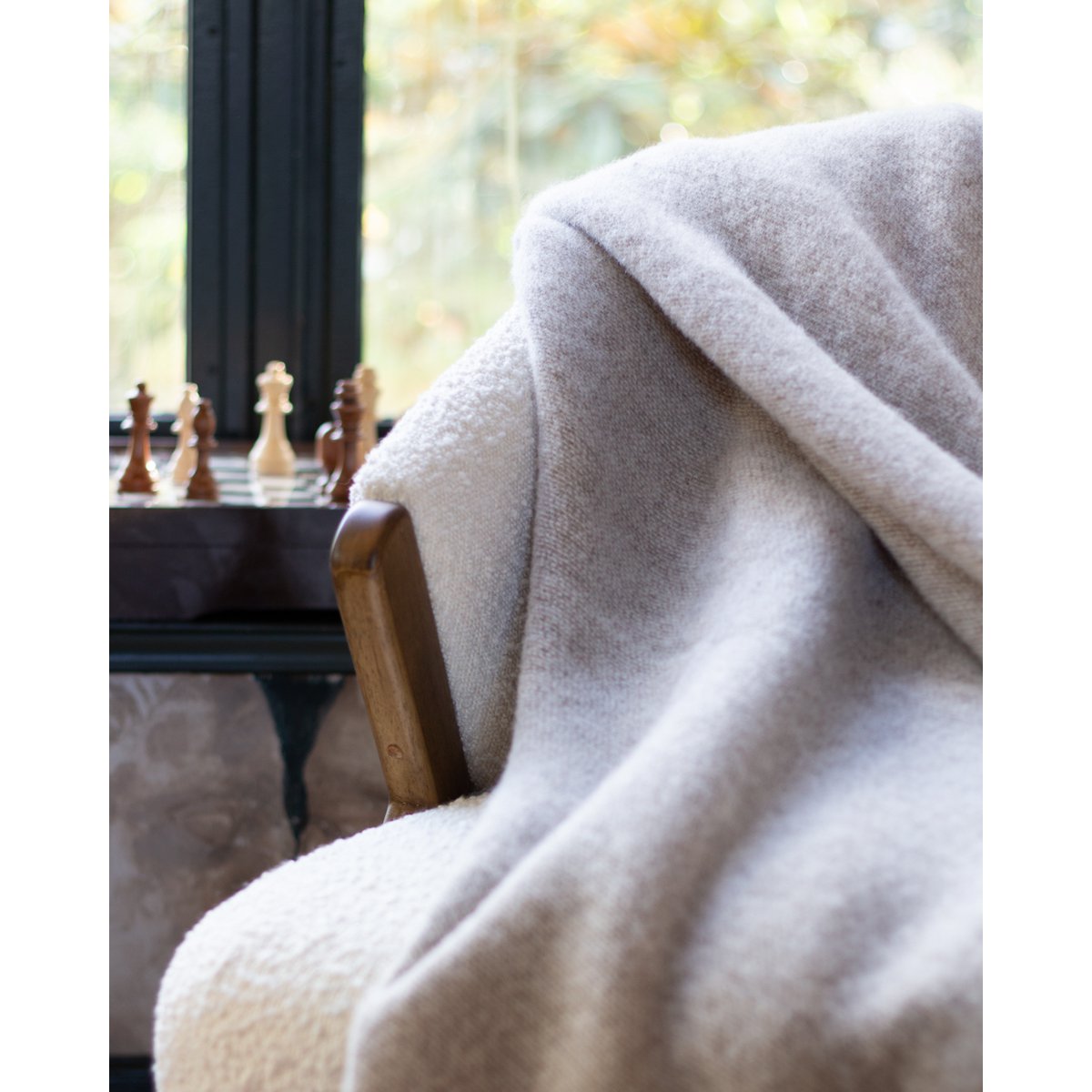 Light gray and beige blanket draped over a chair with a chessboard in the background