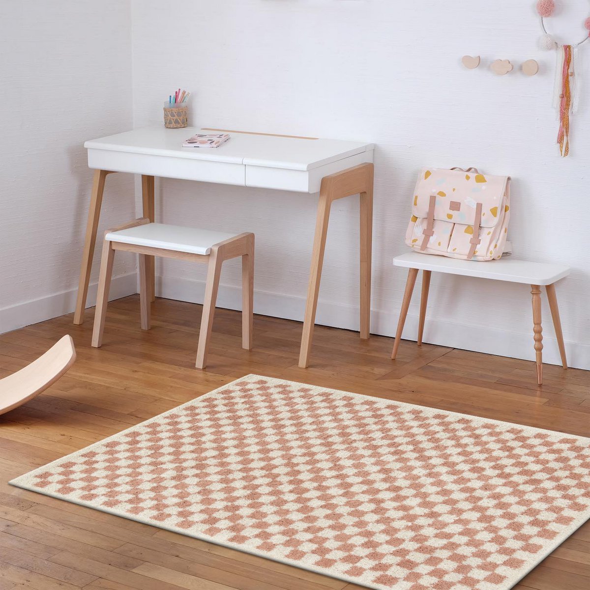 Children's room with a white desk, chair, and small table with a bag on a wooden floor.