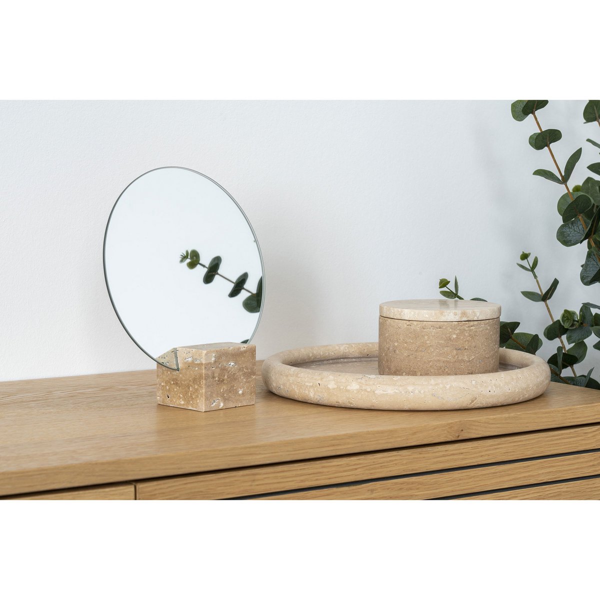 Decorative items including a round mirror, box, and tray on a wooden surface with a plant in the background.