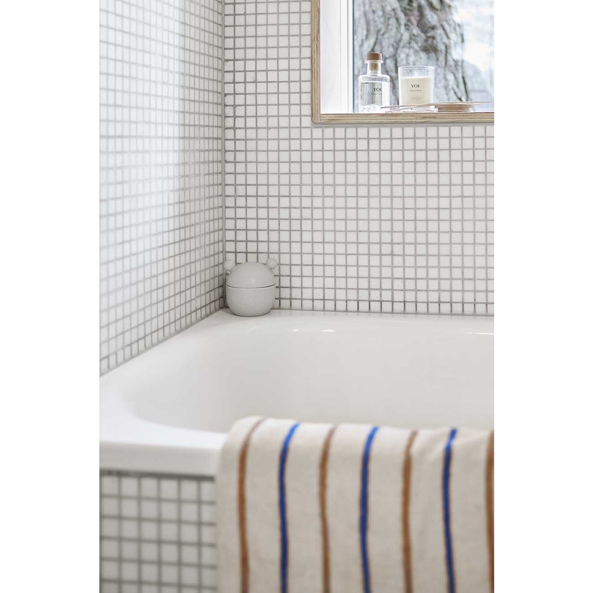 Bathroom with white bathtub and tiled walls, featuring a striped towel.
