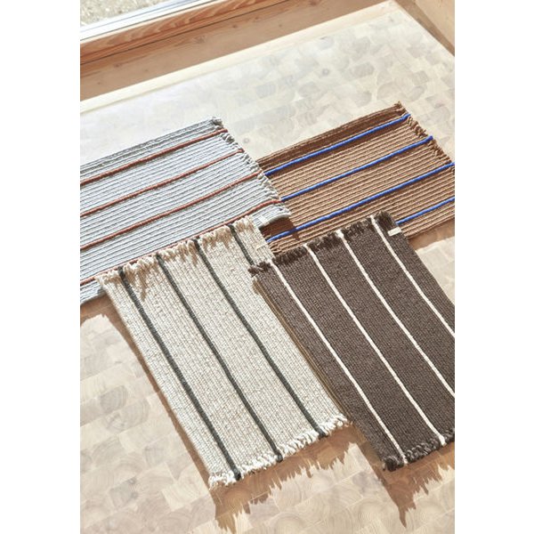 Set of woven bath mats with striped patterns on a wooden surface.
