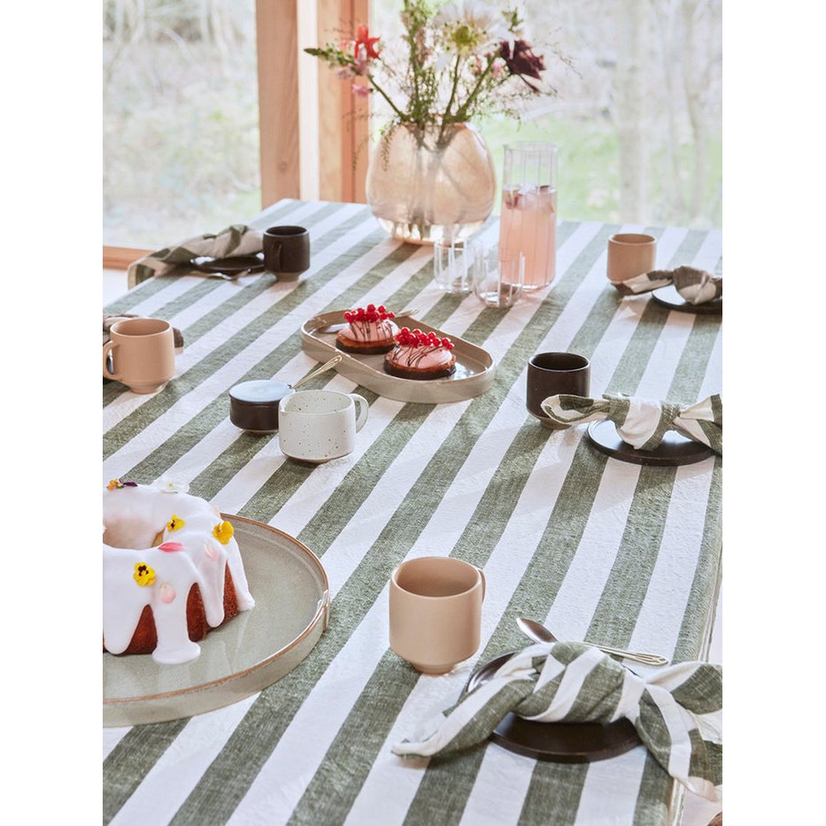 Dining table with striped tablecloth, cups, plates, and a cake.