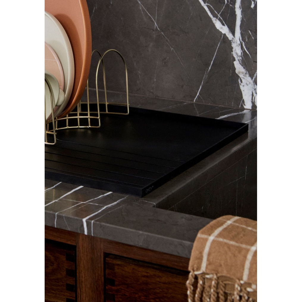 Black marble countertop with a gold dish rack and plates against a dark marble wall.