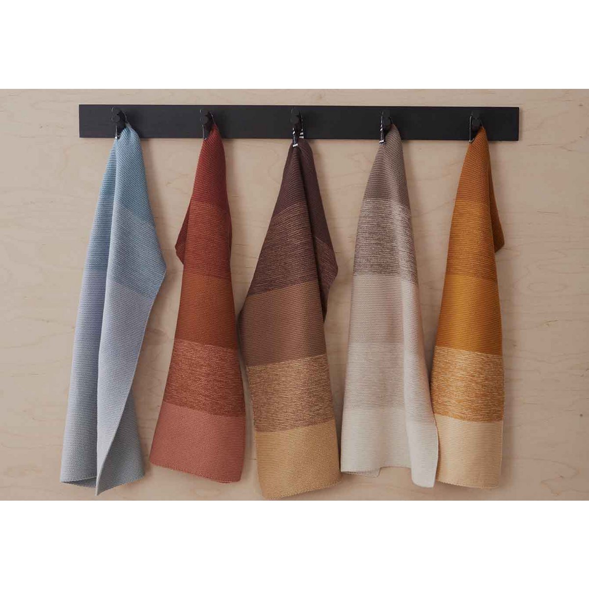 Five gradient towels hanging on a black rack against a wooden wall.