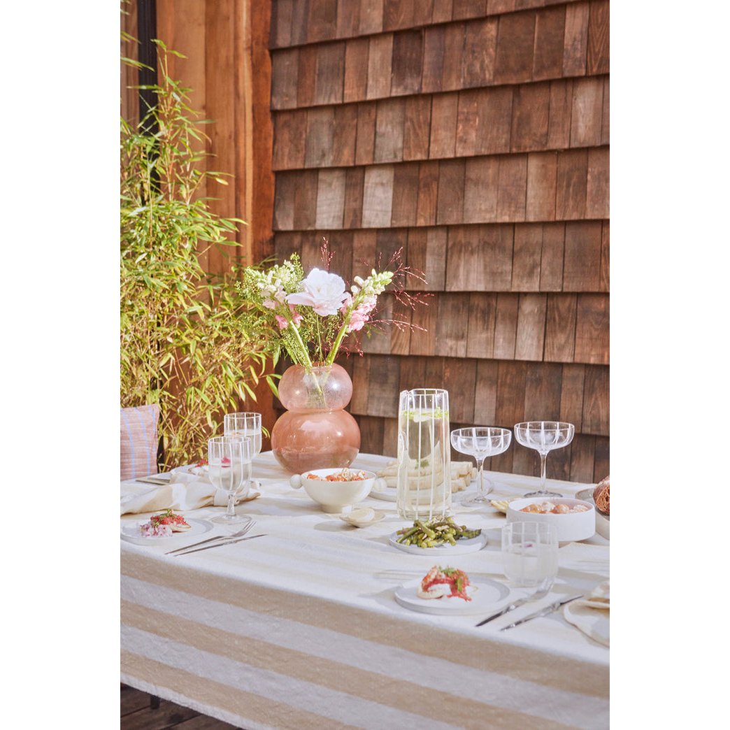 Outdoor table setting with a glass carafe and floral arrangement against a wooden wall.