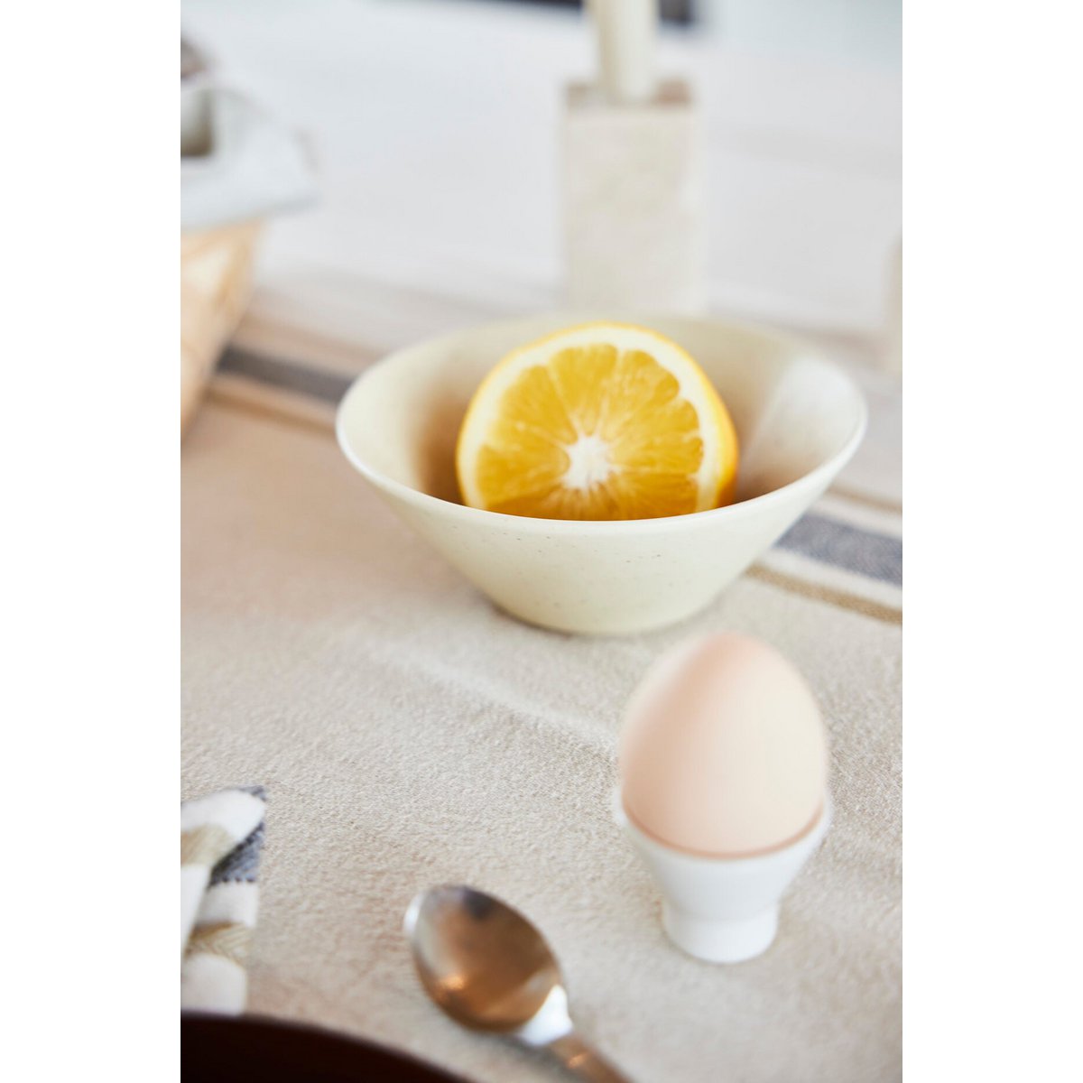 White bowl with a sliced orange and an egg on a kitchen counter.